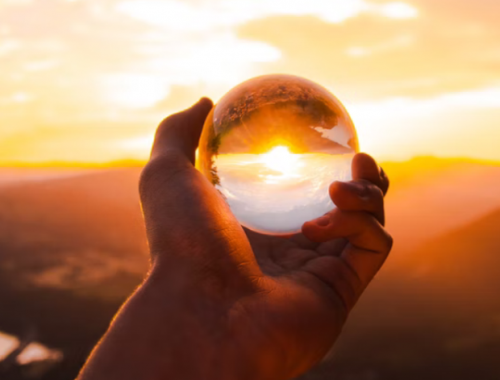 Hand holding a transparent glass ball with sunset background