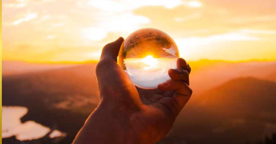 Hand holding a transparent glass ball with sunset background